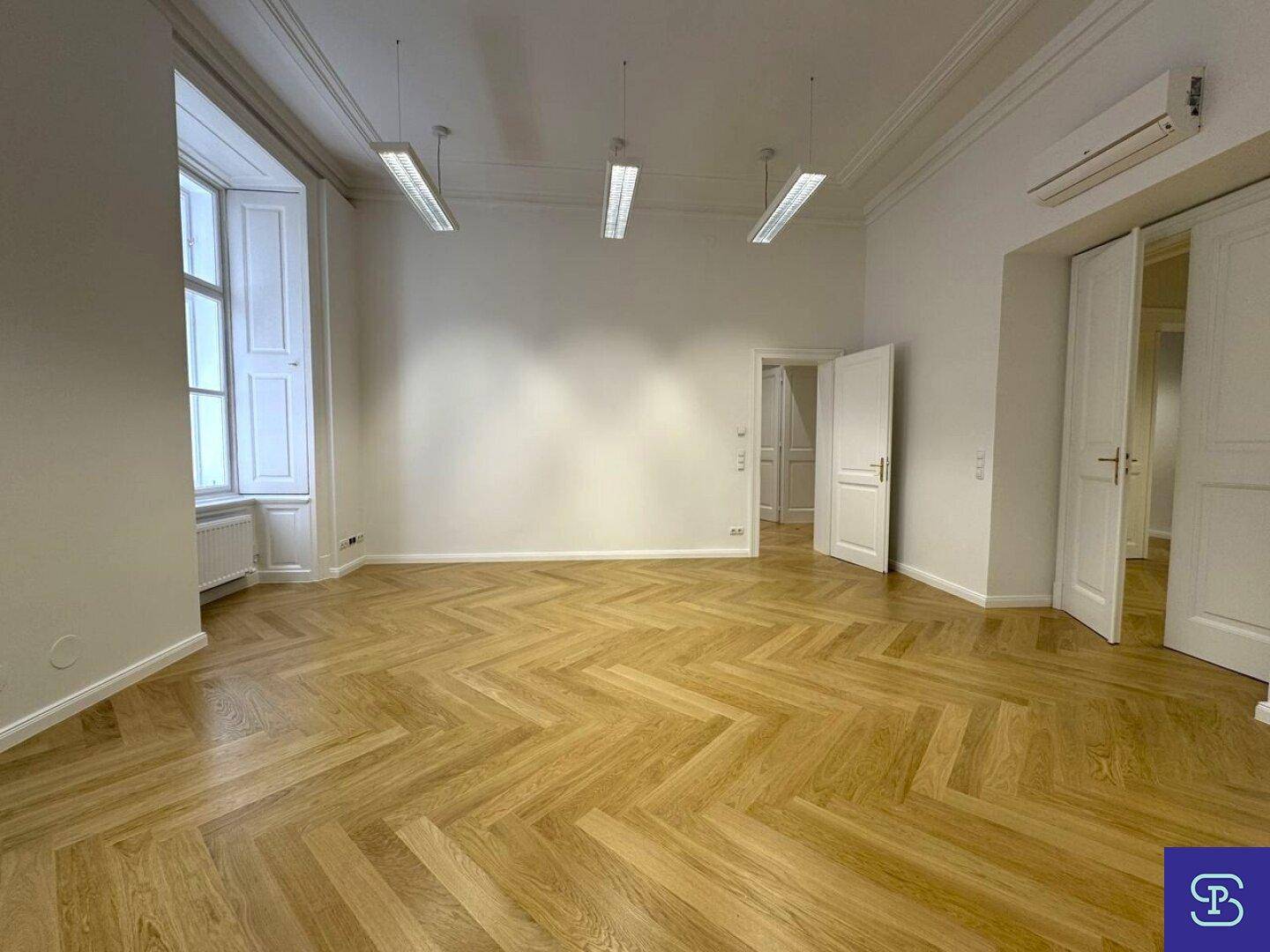 Heller Büroraum mit Fischgrätparkett, hohen Decken und Klimaanlage, ideal für ein produktives Arbeitsumfeld.
