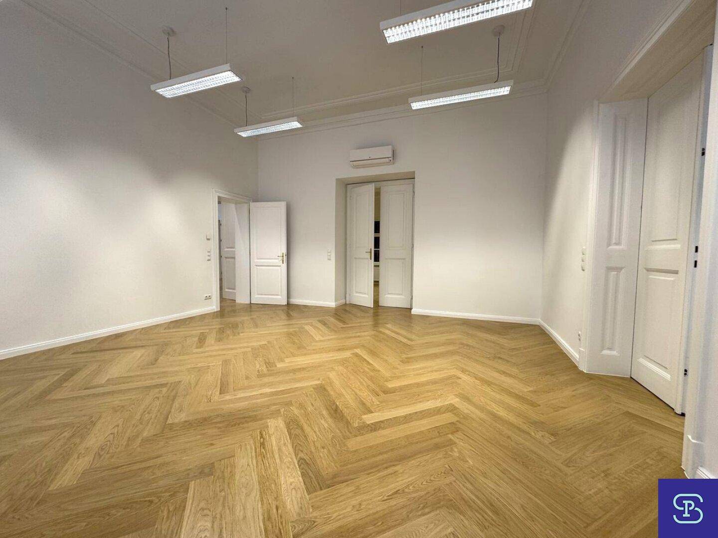 Großer Büroraum mit Fischgrätparkett, hohen Decken und Klimaanlage, bereit zur individuellen Einrichtung.