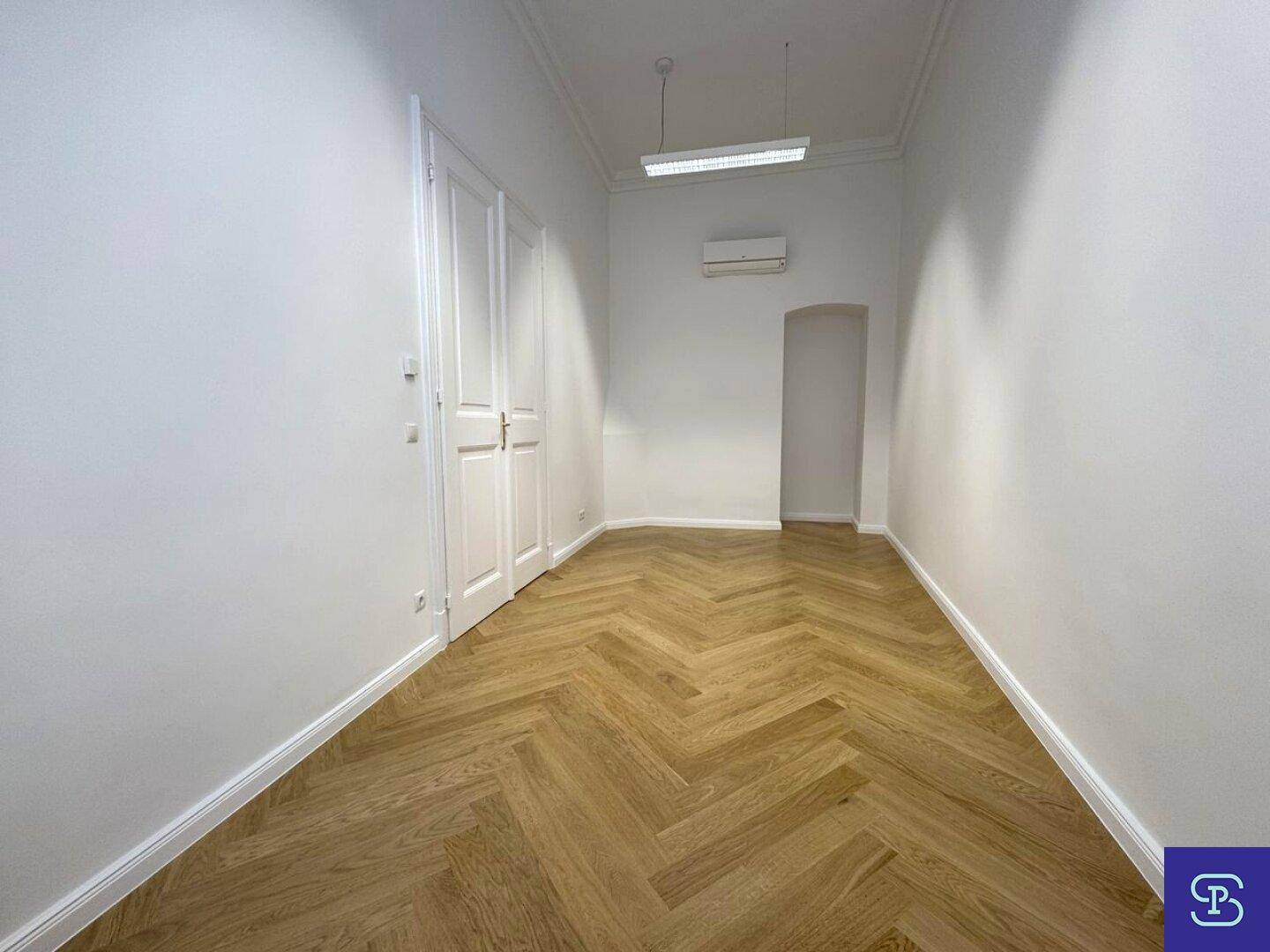 Heller Büroraum mit Fischgrätparkett, hohen Decken und Klimaanlage, ideal für ein Einzelbüro oder Besprechungszimmer.
