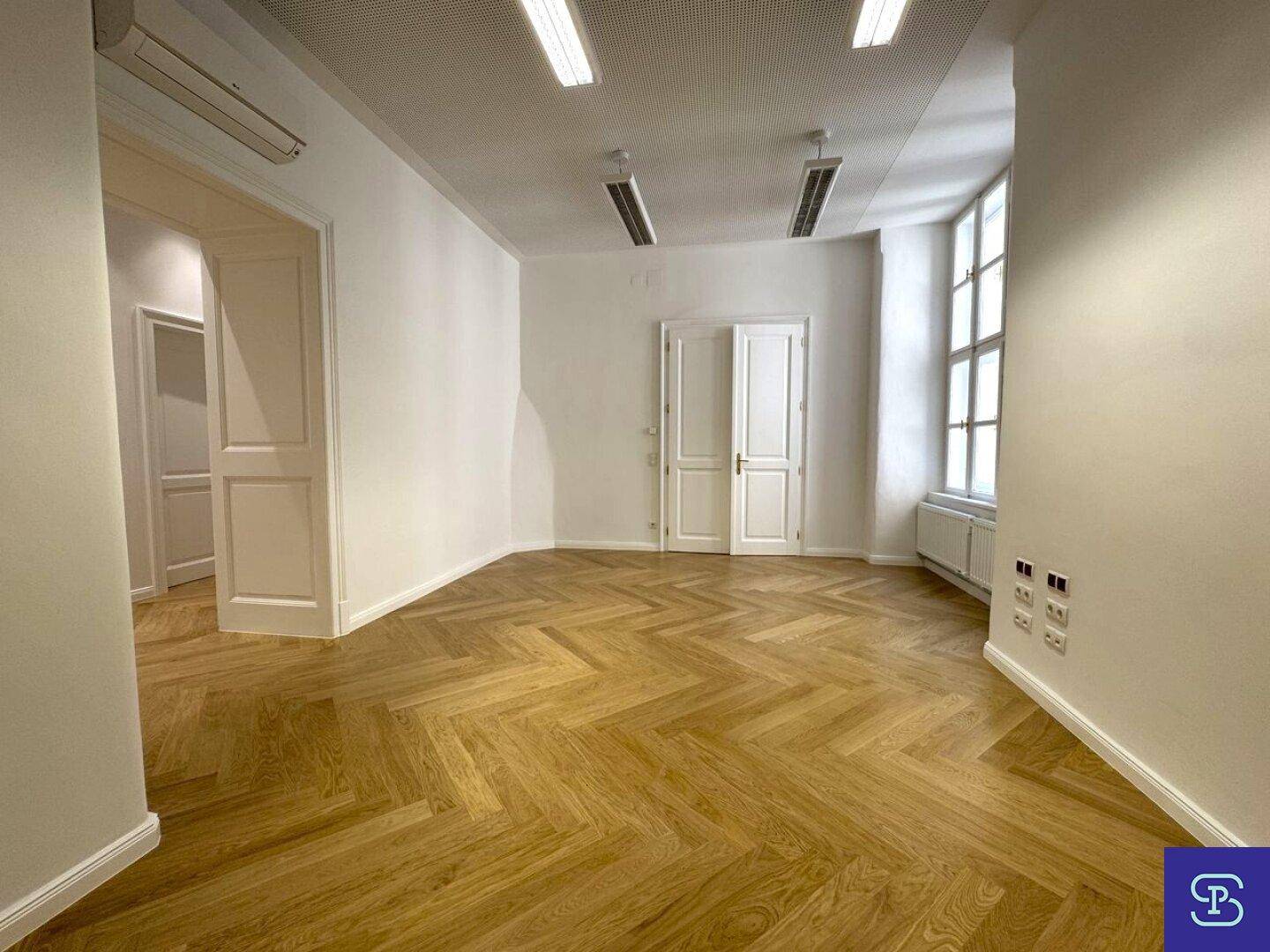 Heller Büroraum mit Fischgrätparkett, hohen Decken und Klimaanlage, ideal für ein modernes Büro.