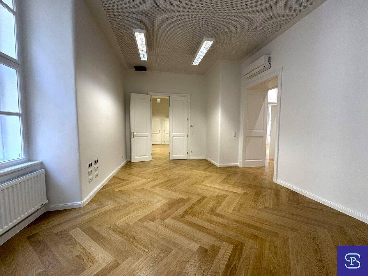 Großer Büroraum mit Fischgrätparkett, hohen Decken und Klimaanlage, bereit zur individuellen Gestaltung.