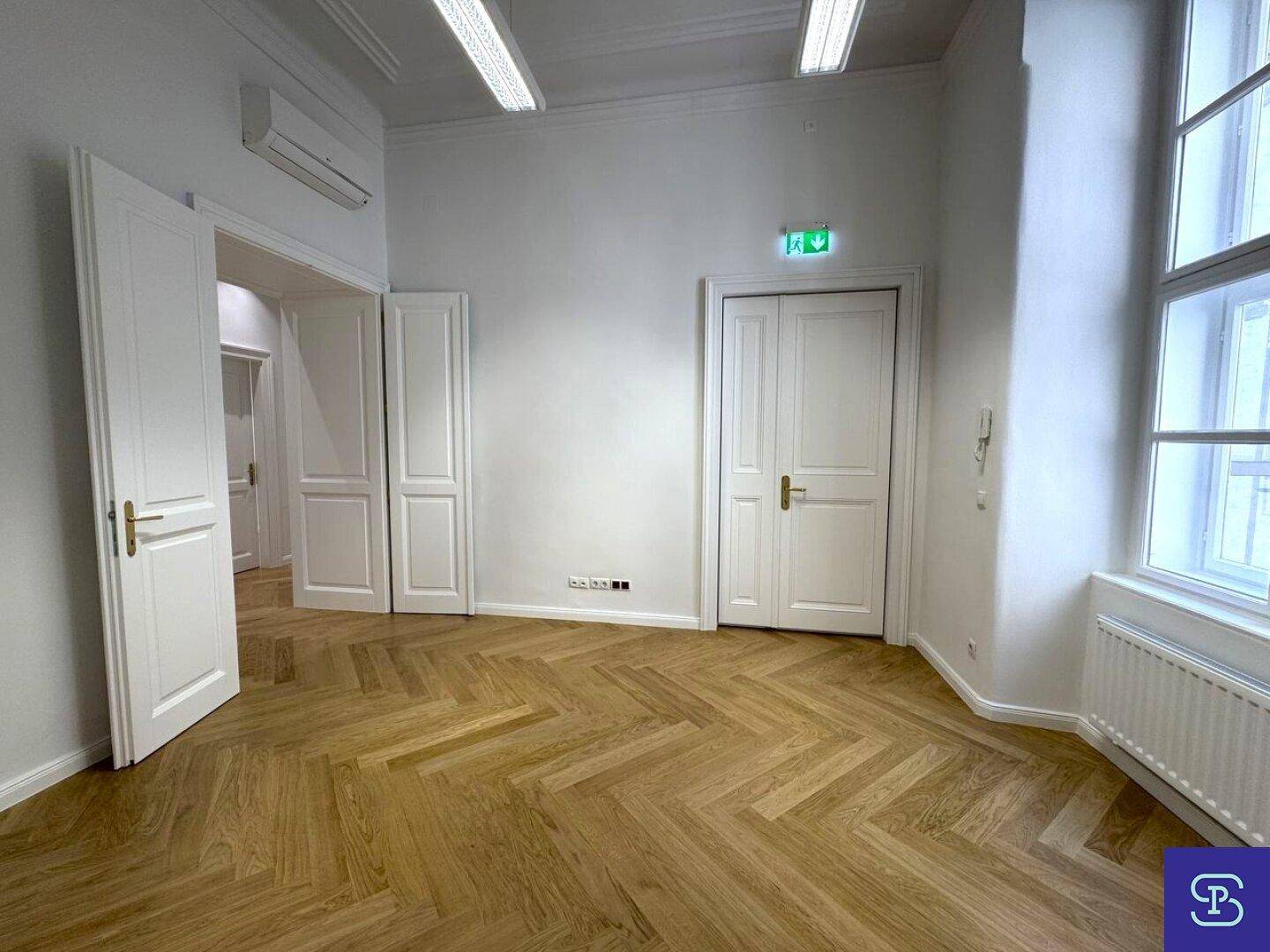 Helles Büro mit Fischgrätparkett, hohen Decken und Klimaanlage, bereit für die Einrichtung.