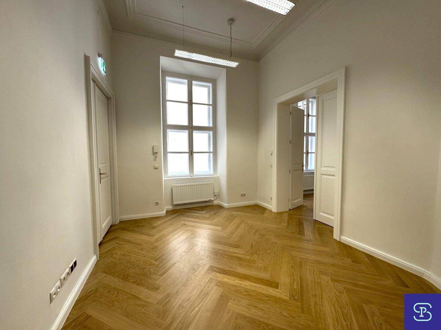 Geräumiges Büro mit Fischgrätparkett, Stuckdecke und großen Fenstern, die viel Licht hereinlassen.