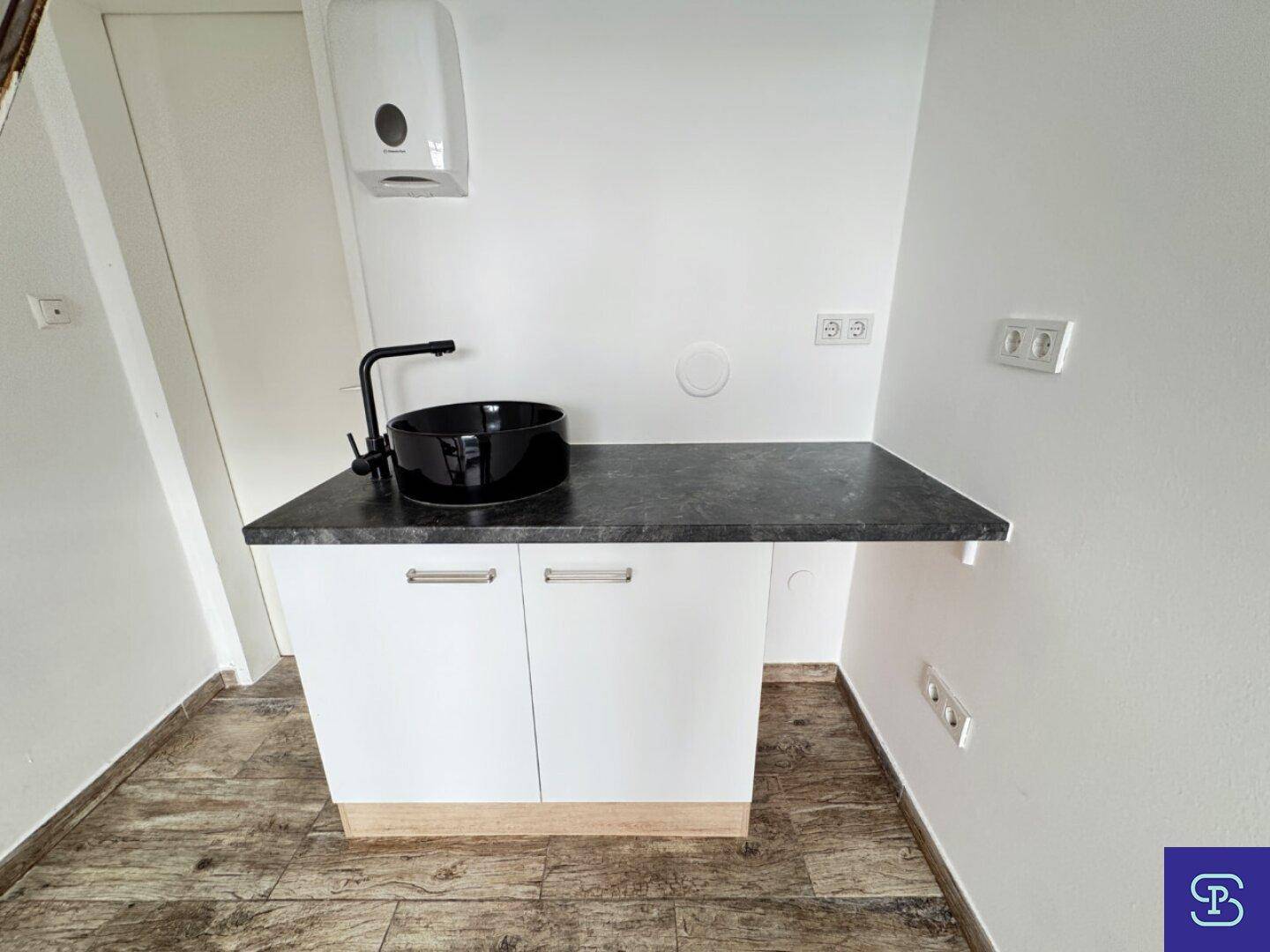 Moderne Küchenzeile mit schwarzem Aufsatzwaschbecken und dunkler Arbeitsplatte, ideal für kleine Gewerbeflächen.