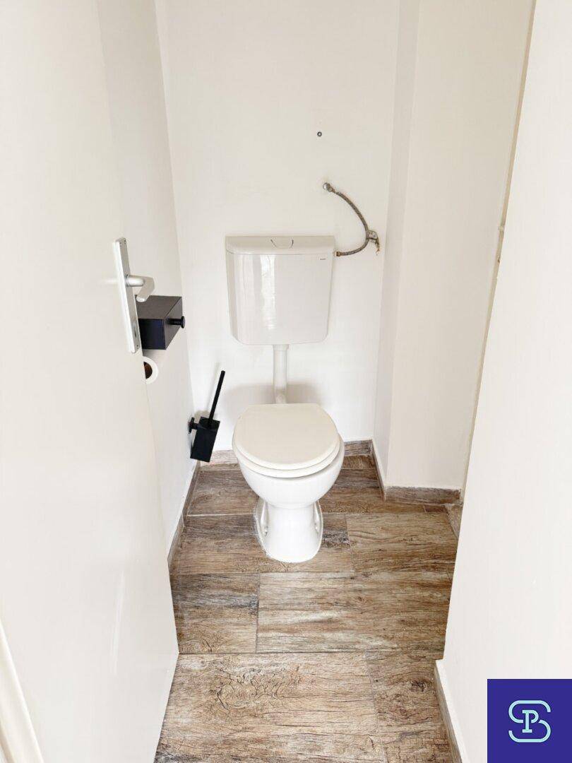 Schmale Toilette mit weißem WC und modernen Fliesenboden, sauber und funktional gestaltet.
