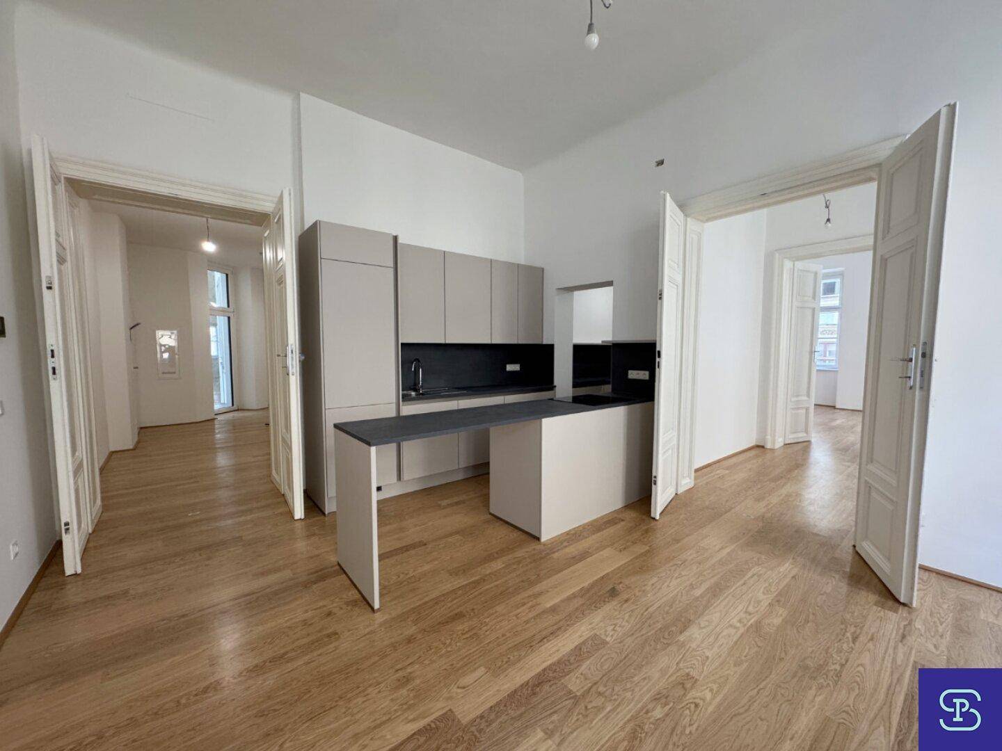 Offene Küche mit integrierten Geräten und Holzboden, verbunden mit weiteren Räumen durch Flügeltüren.