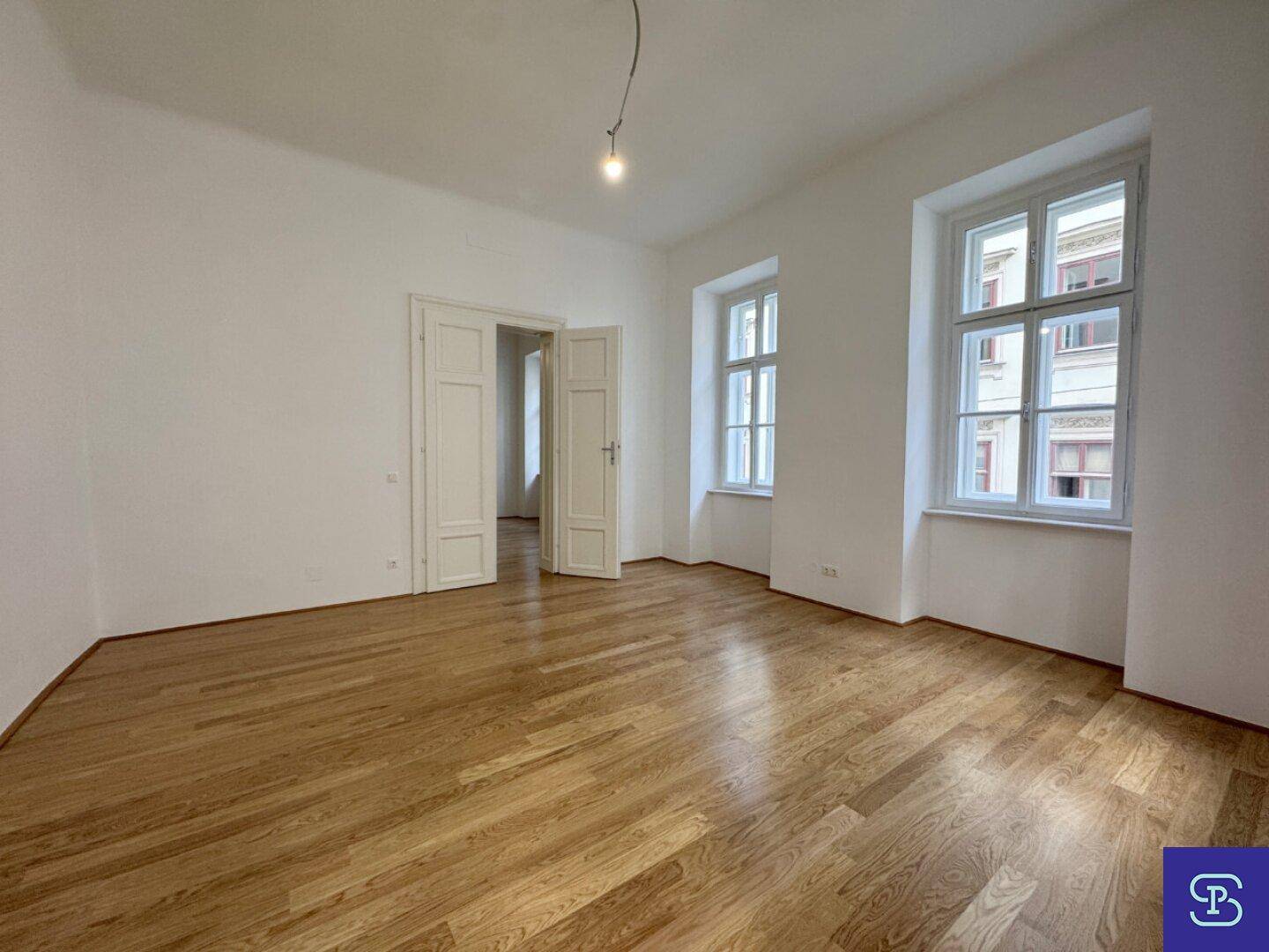 Großes, helles Wohnzimmer mit Holzboden und hohen Fenstern, bereit zur individuellen Gestaltung.