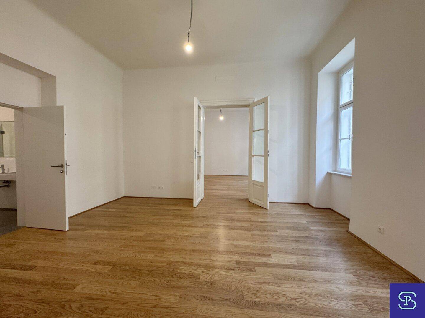 Helles Wohnzimmer mit Holzboden und Zugang zu weiteren Räumen durch Flügeltüren.