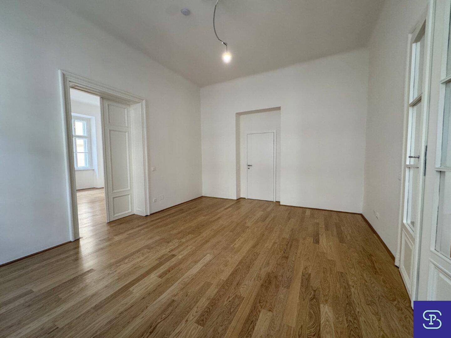 Helles Wohnzimmer mit Holzboden und einer Tür, die zu einem weiteren Raum führt.