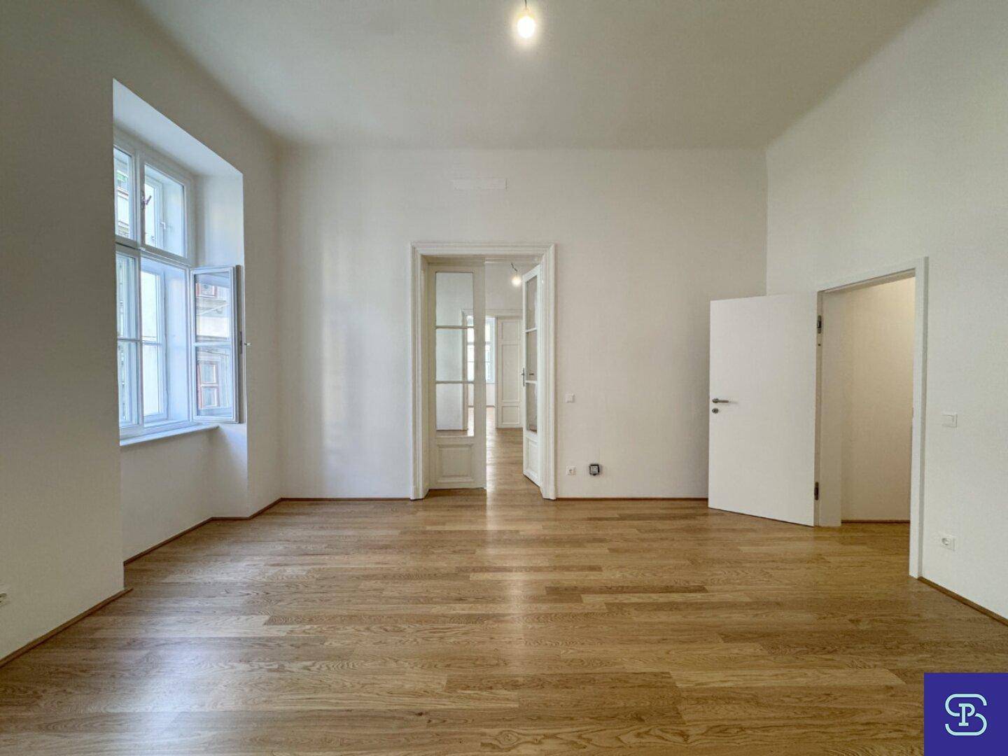 Helles Wohnzimmer mit Holzboden und Zugang zu weiteren Räumen durch Flügeltüren.
