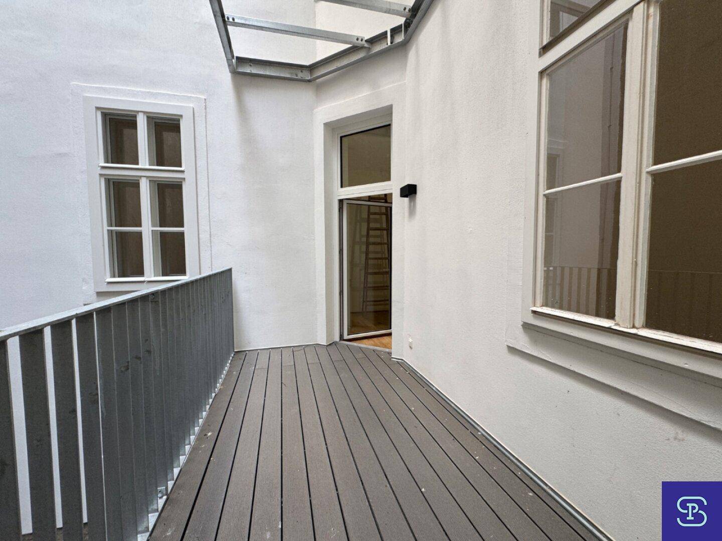 Moderner Balkon mit Holzdielen und Metallgeländer, überdacht für zusätzlichen Komfort.
