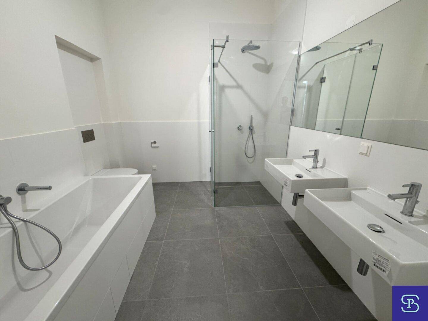 Modernes Badezimmer mit Badewanne, großer Dusche und Doppelwaschbecken, hell gefliest.