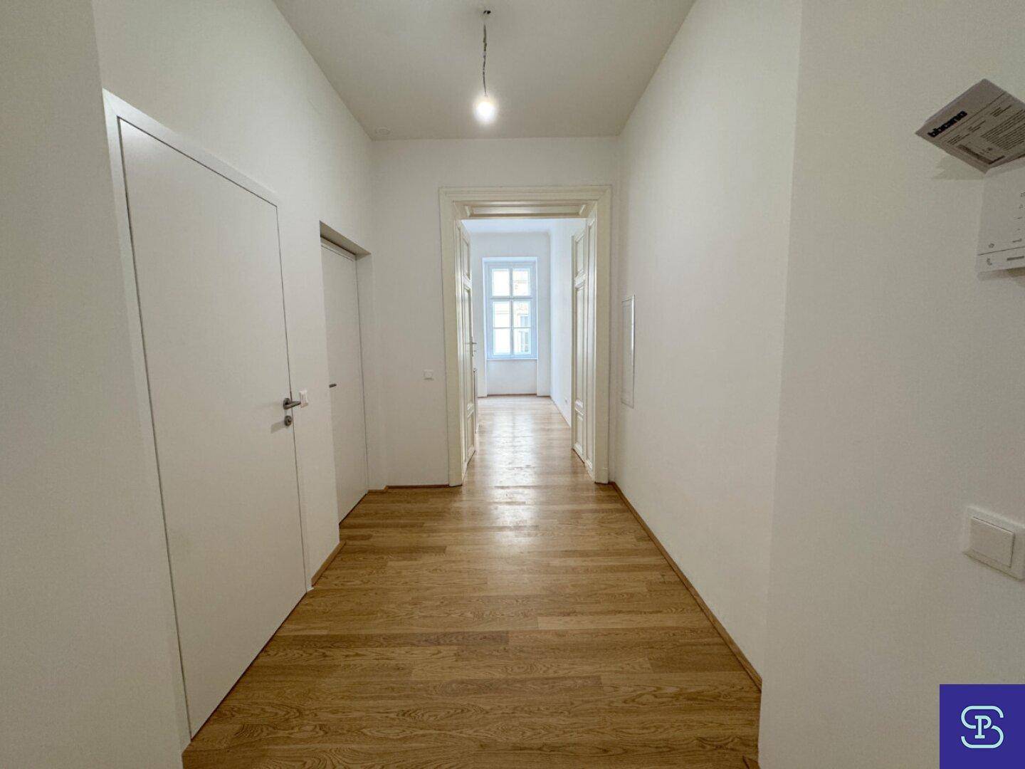 Heller Flur mit Holzboden und hohen Türen, der zu weiteren Räumen führt.