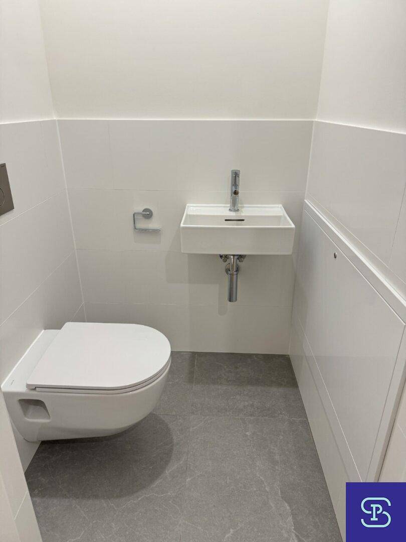 Separates Gäste-WC mit wandhängendem WC und kleinem Waschbecken, modern gefliest.