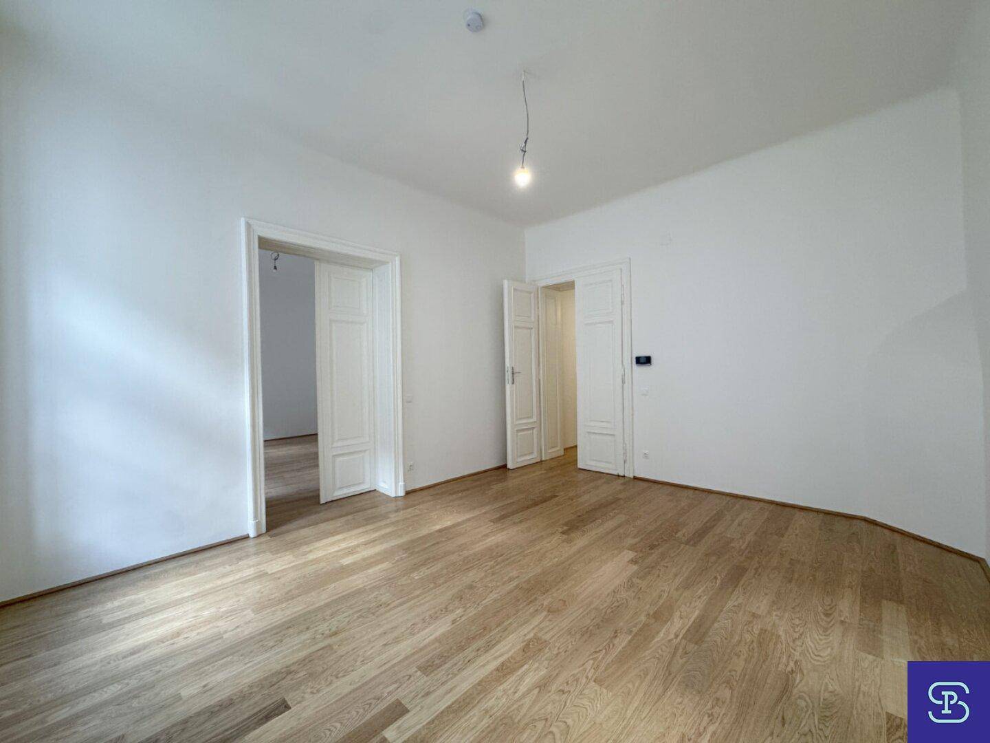 Geräumiges Zimmer mit klassischem Holzboden und mehreren Türen zu angrenzenden Räumen.
