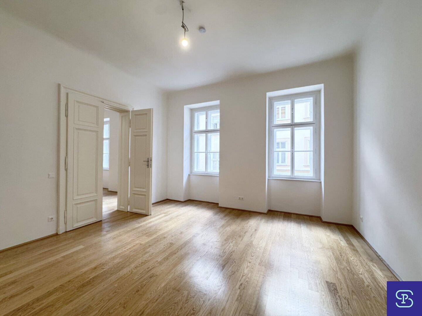 Lichtdurchflutetes Zimmer mit elegantem Holzboden und hohen Fenstern, ideal für Wohnzwecke.