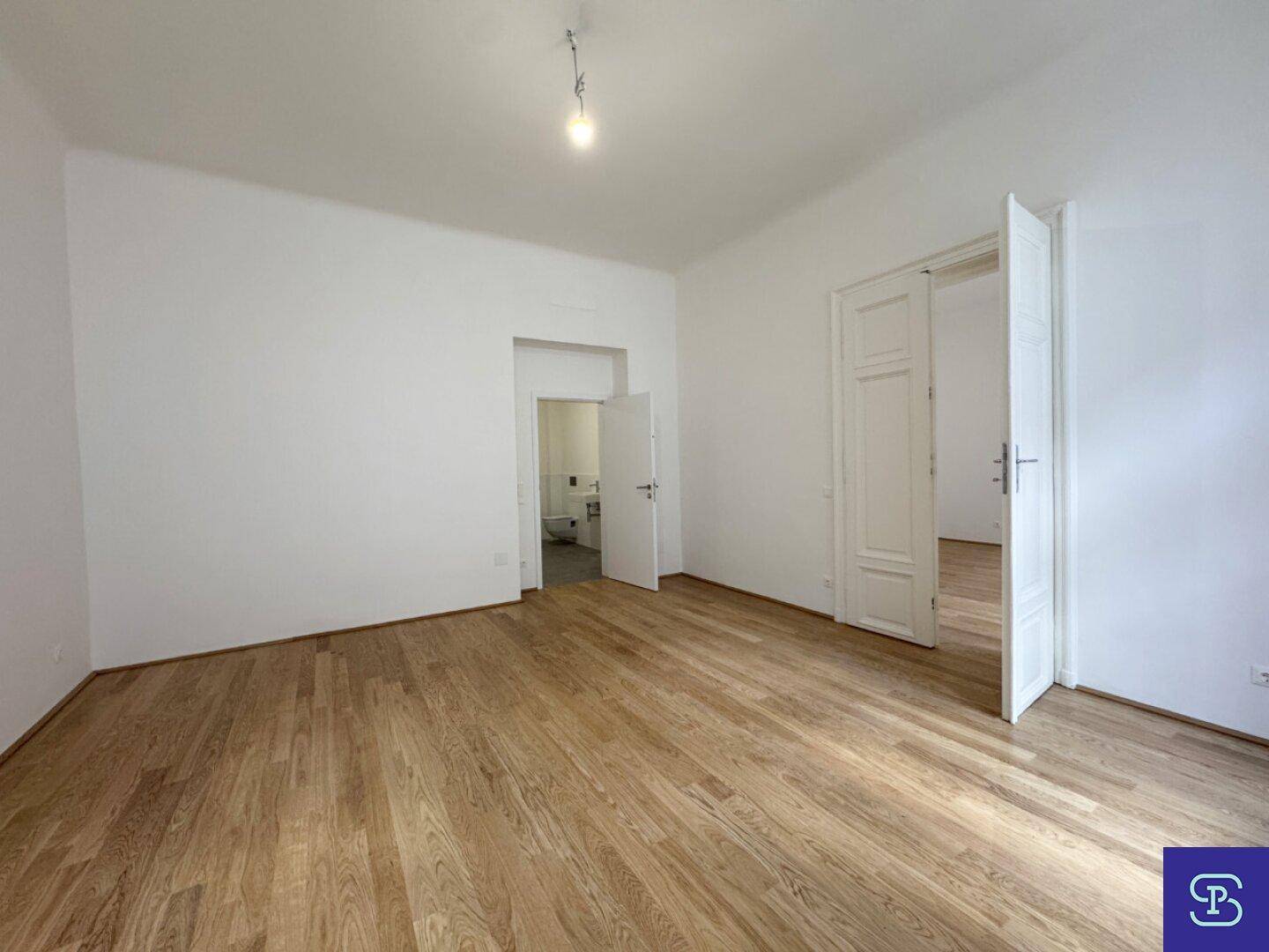 Geräumiges Zimmer mit Holzboden und Zugang zu einem modernen Badezimmer.