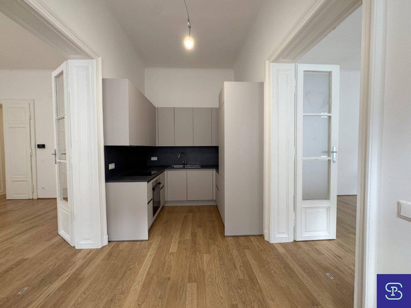 Heller Wohnbereich mit Holzboden und Blick auf eine kompakte, moderne Küchenzeile.