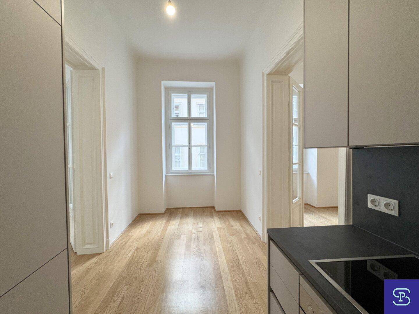 Blick von der Küchenzeile in ein helles Zimmer mit Holzboden und großem Fenster.