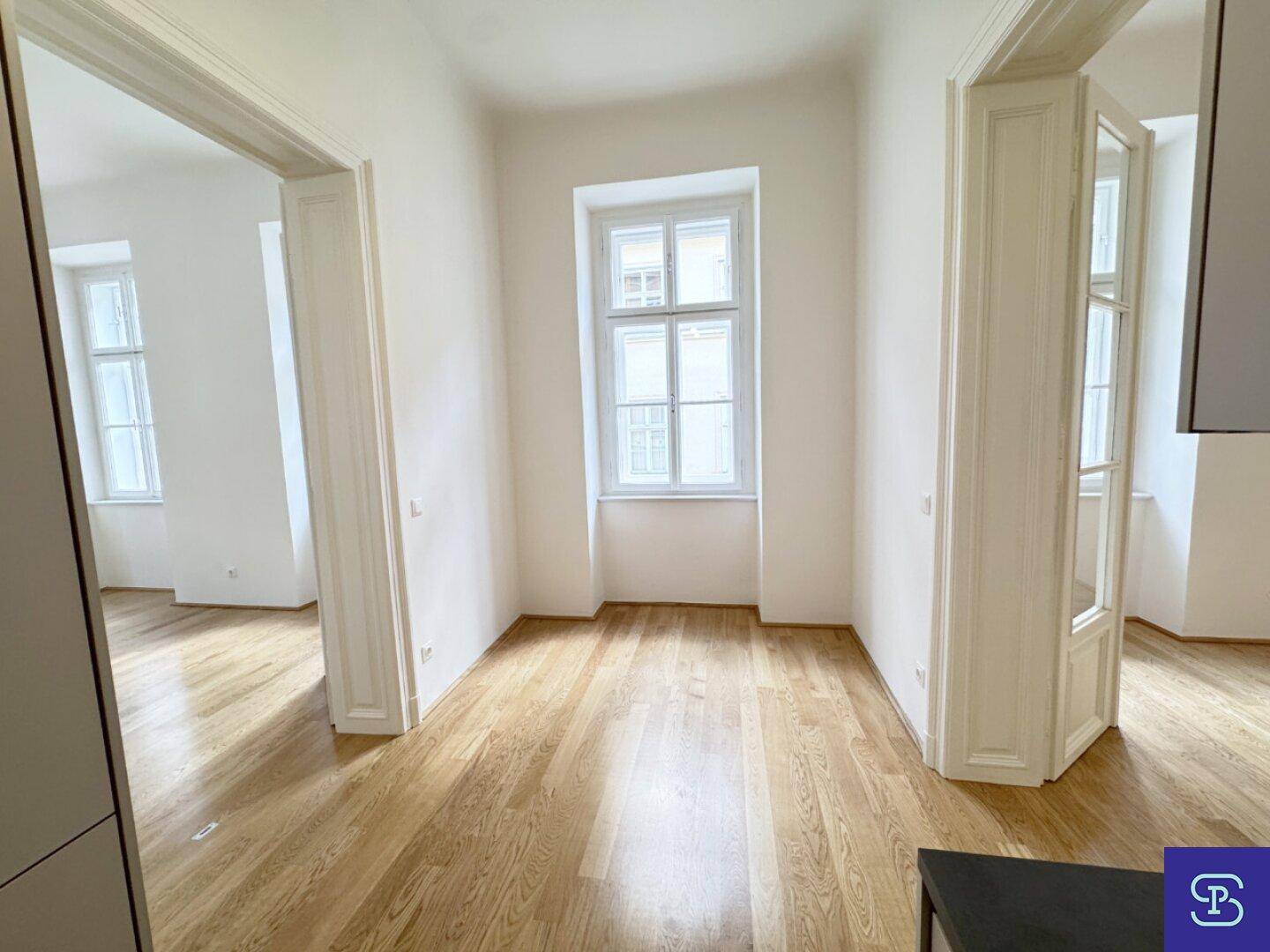 Heller Raum mit Holzboden und Fenster, gesehen vom Bereich der Küchenzeile aus.