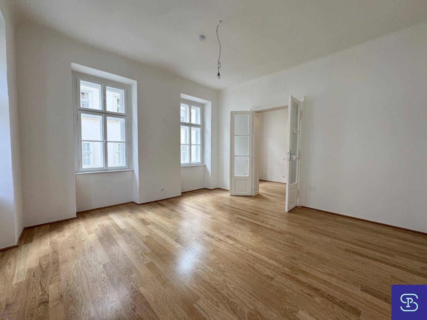 Geräumiges Zimmer mit Holzboden, hohen Fenstern und Doppeltüren, ideal für vielfältige Nutzung.