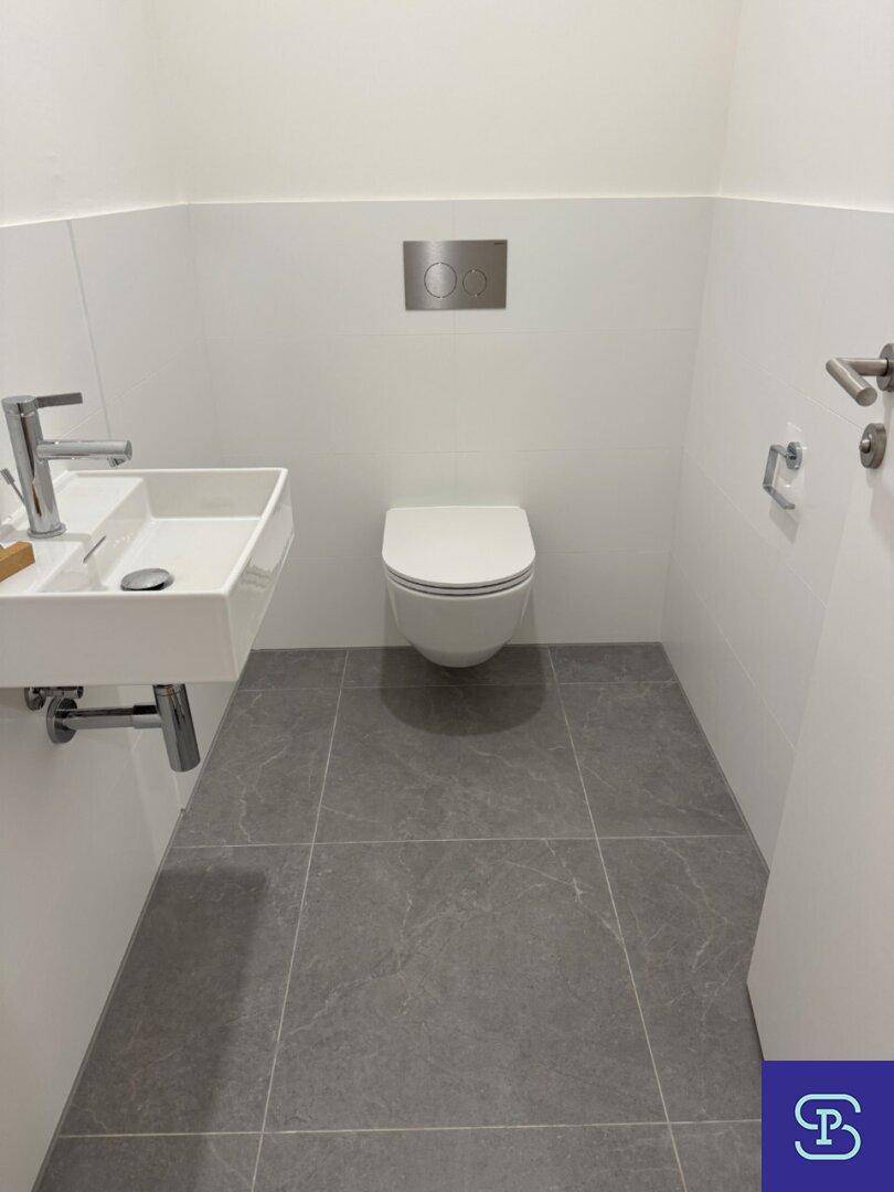 Modernes Gäste-WC mit wandhängendem WC und kleinem Waschbecken auf grauem Fliesenboden.