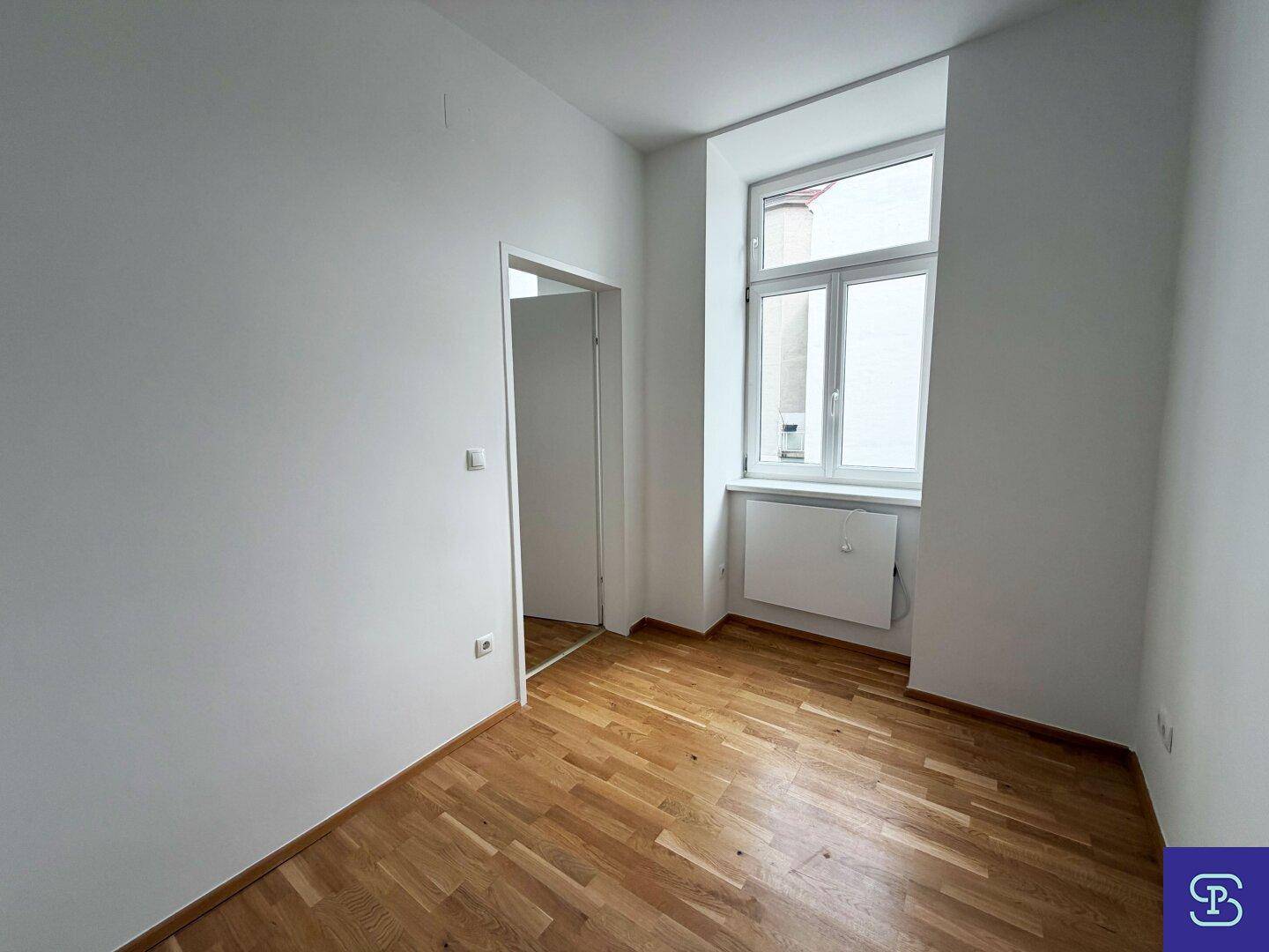 Helles Zimmer mit Parkettboden und einem Fenster, das viel Tageslicht hereinlässt.