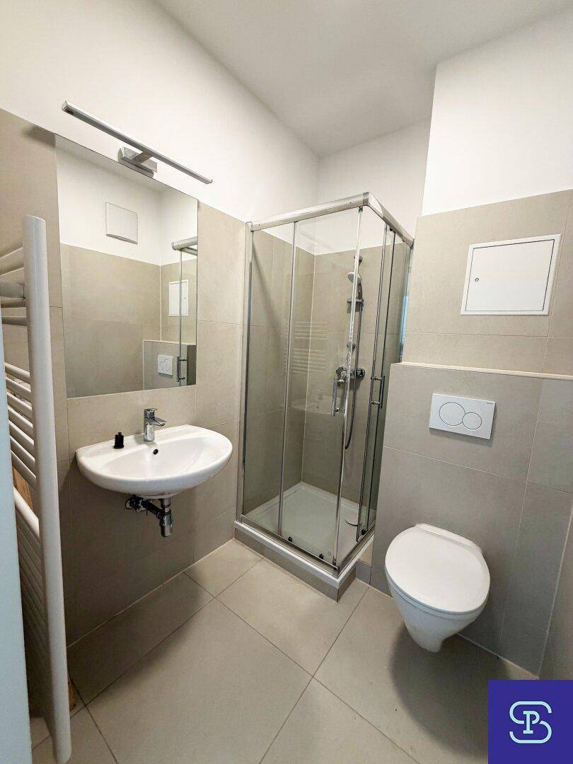 Modernes Badezimmer mit Duschkabine, Waschbecken, WC und hellen Fliesen an Wänden und Boden.