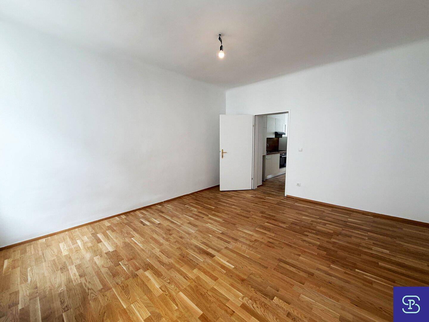 Helles Wohnzimmer mit Parkettboden und offener Tür zur angrenzenden Küchenzeile.