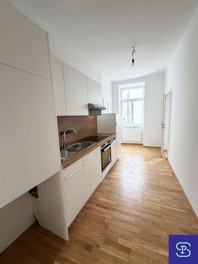 Kompakte Küchenzeile mit weißen Oberschränken, Holzarbeitsplatte und Fenster für Tageslicht.
