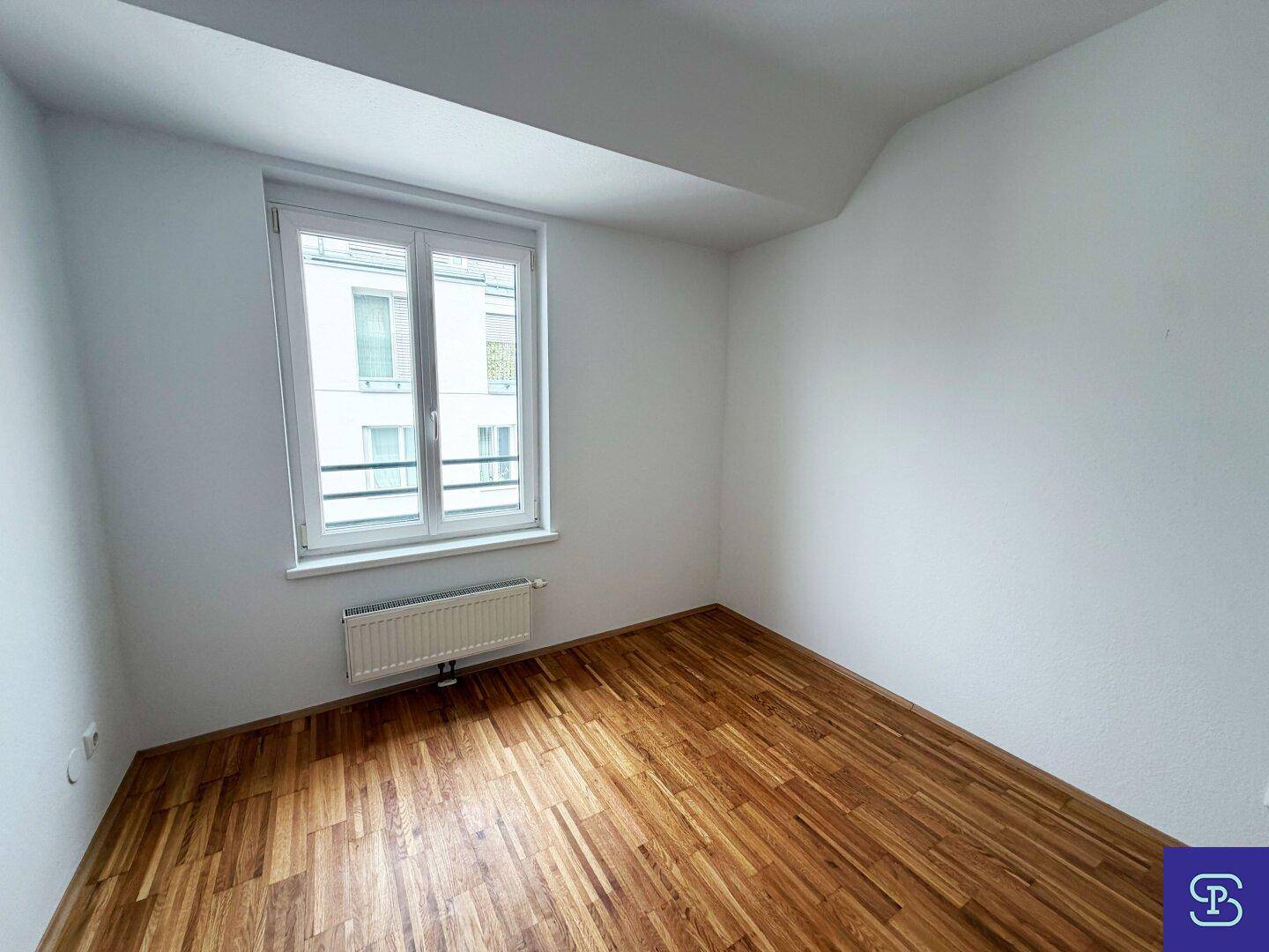 Helles Zimmer mit Parkettboden und großem Fenster, ideal als Schlaf- oder Arbeitszimmer.