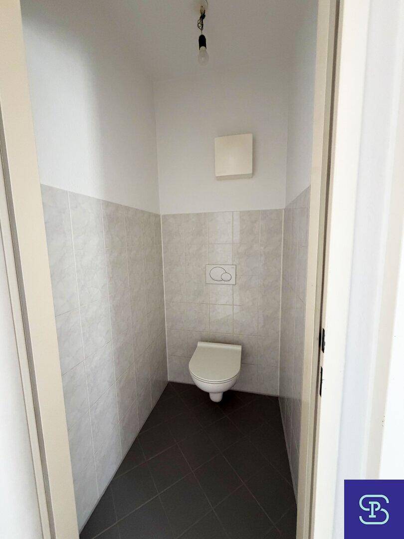 Separates WC mit Wand-WC und Fliesen an den Wänden, funktional und sauber.