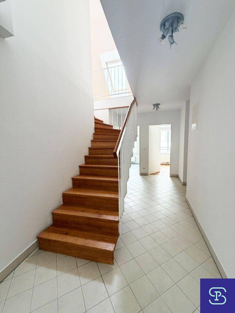 Geräumiger Flur mit Holztreppe und hellem Fliesenboden, führt zu den oberen Etagen.