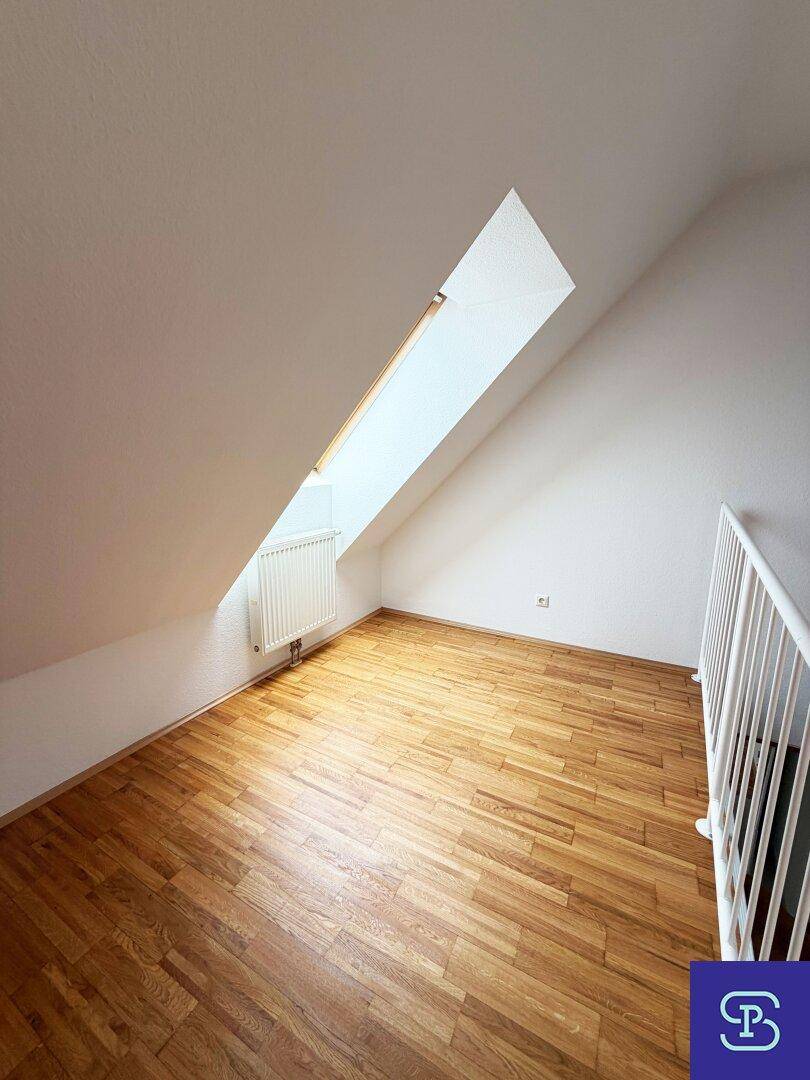 Dachzimmer mit Parkettboden und schrägem Dachfenster, bietet viel natürliches Licht.
