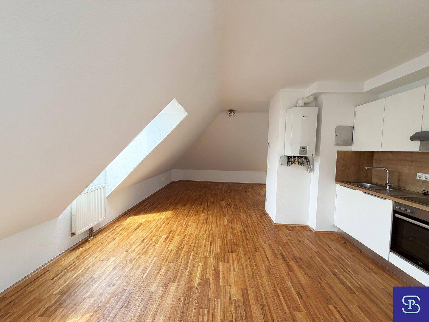 Heller Wohnbereich mit integrierter Küchenzeile, Parkettboden und schrägem Dachfenster.