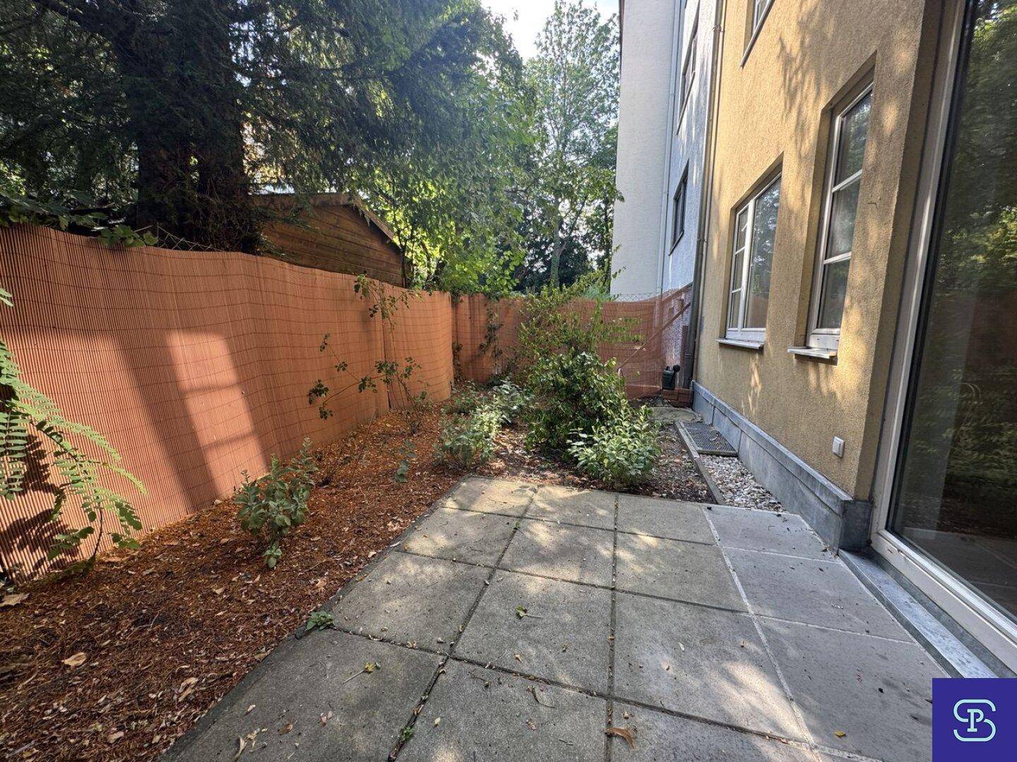 Seitlicher Blick auf den Gartenbereich mit Terrasse und der Gebäudefassade.