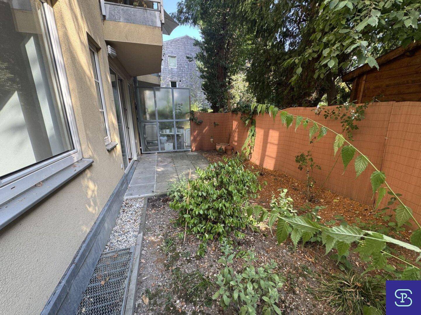 Gartenbereich mit Terrasse und einem kleinen verglasten Anbau am Gebäude.
