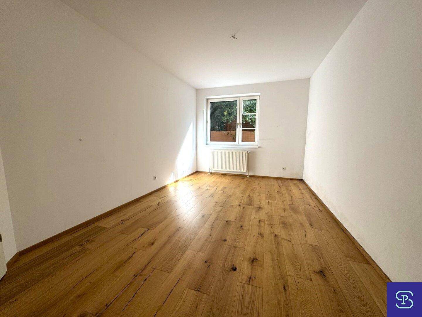 Helles Schlafzimmer mit Holzboden und einem Fenster mit Blick ins Grüne.