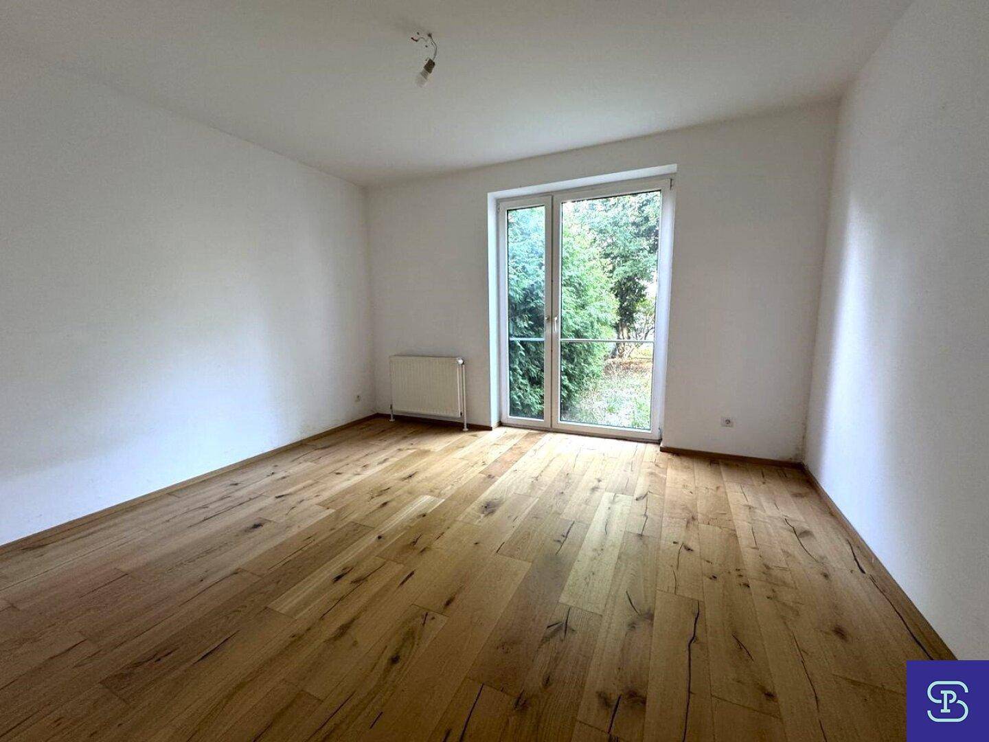 Helles Zimmer mit Holzboden und großer Glastür zum Außenbereich.