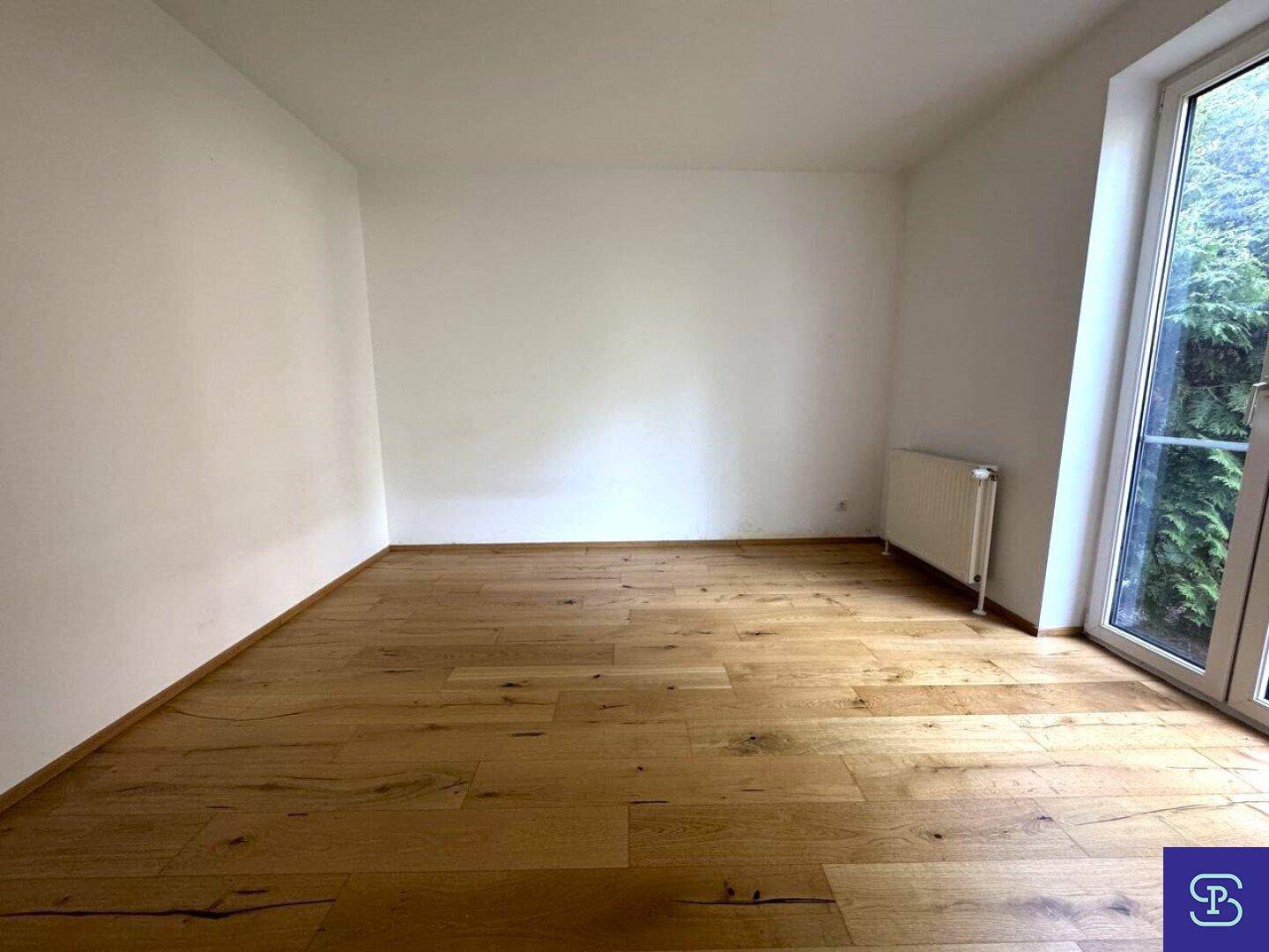 Geräumiges Zimmer mit Holzboden und Zugang zu einem Balkon oder Garten.