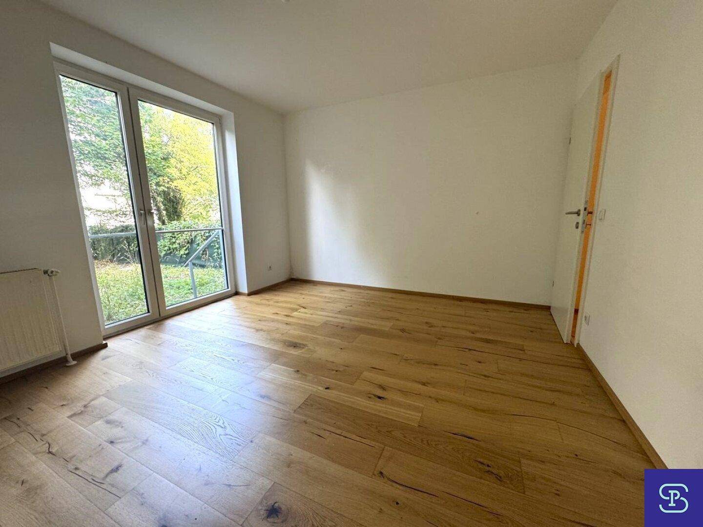 Lichtdurchflutetes Zimmer mit Holzboden und breiter Glastür zum Außenbereich.