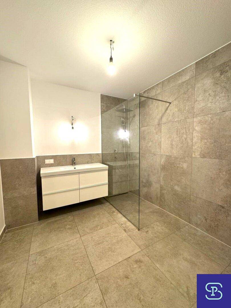Zeitgemäßes Badezimmer mit großformatigen Fliesen, Waschtisch und Glasdusche.