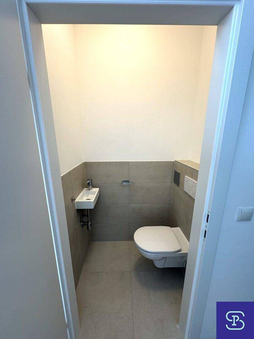 Kleines Gäste-WC mit wandhängender Toilette und Handwaschbecken, modern gefliest.