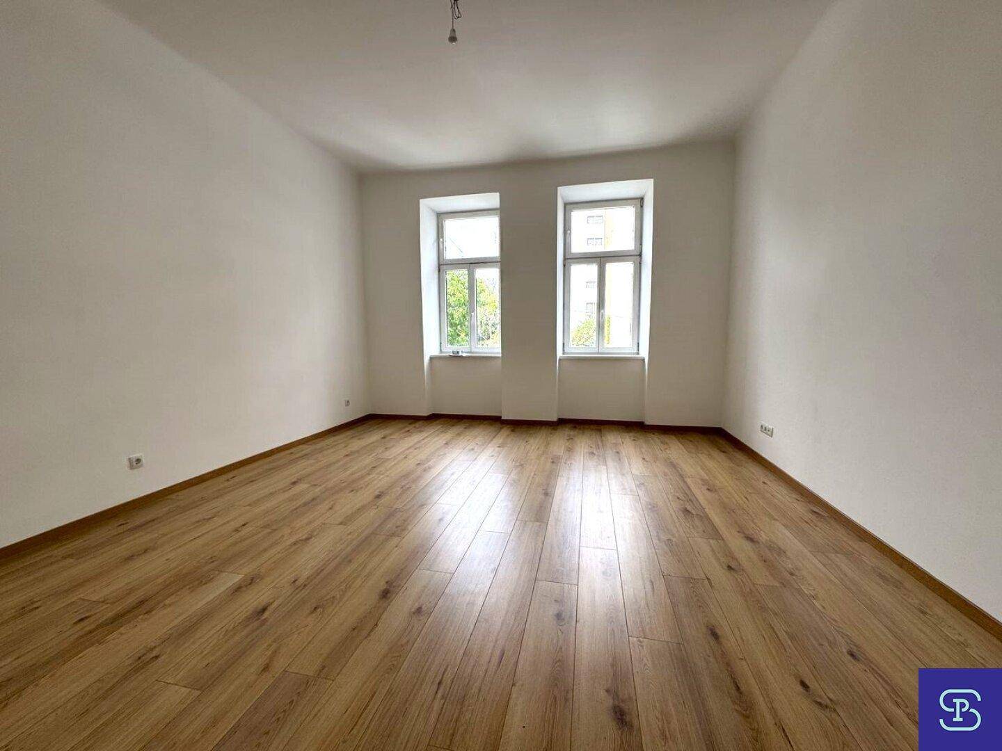 Helles Zimmer mit Laminatboden und zwei Fenstern, die viel Tageslicht hereinlassen.