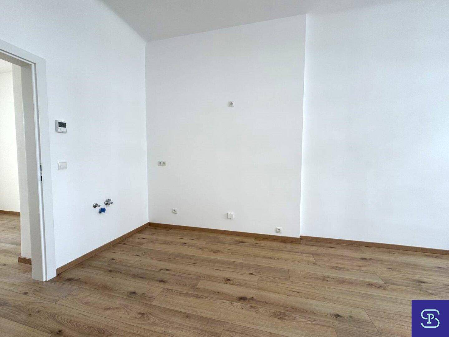 Ecke eines Zimmers mit Laminatboden und Anschlüssen an der Wand, bereit für weitere Installationen.
