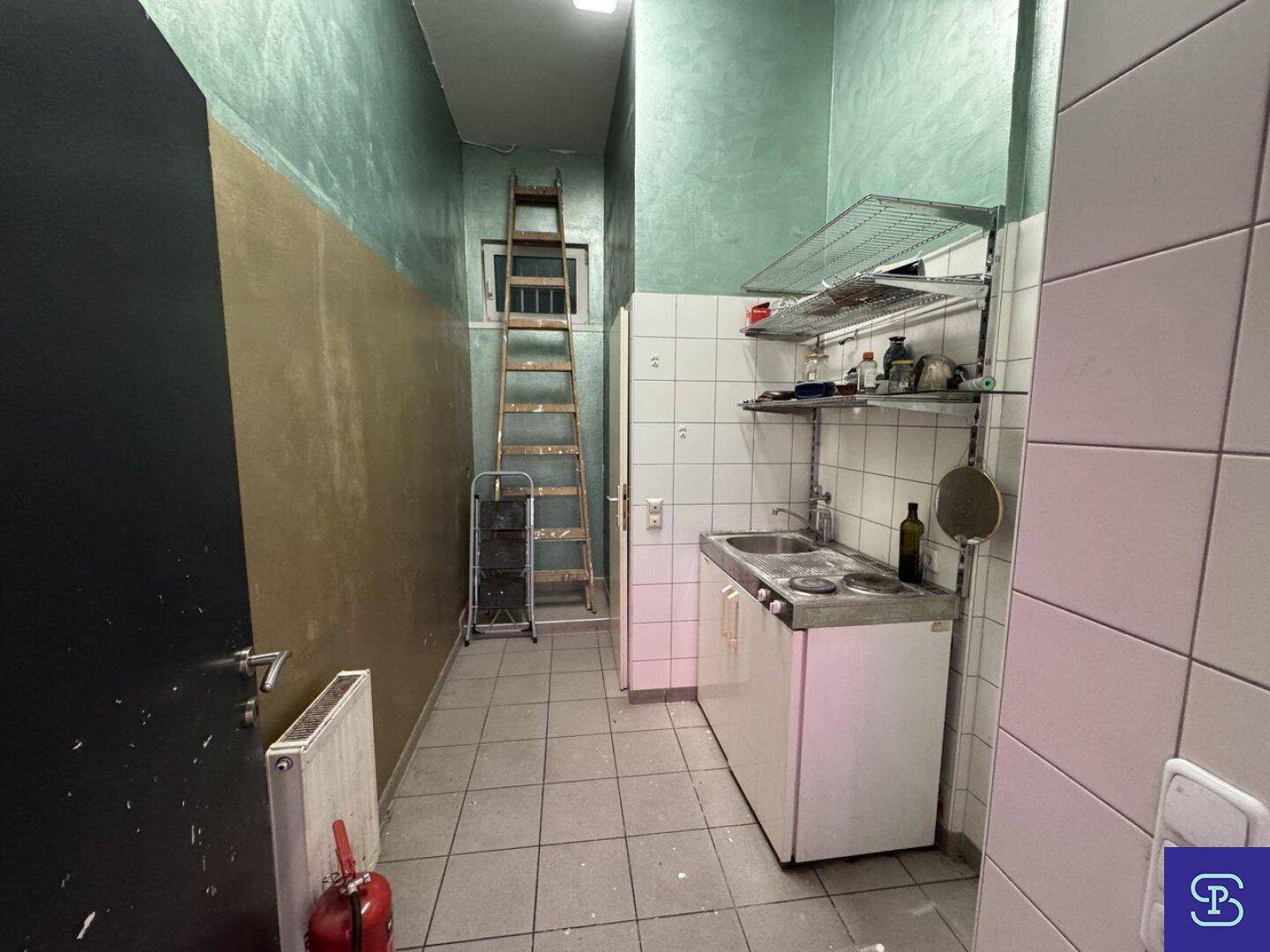 Kleine Küchenzeile mit Spüle, Fliesenwänden und einer Leiter, die zu einem oberen Bereich führt.