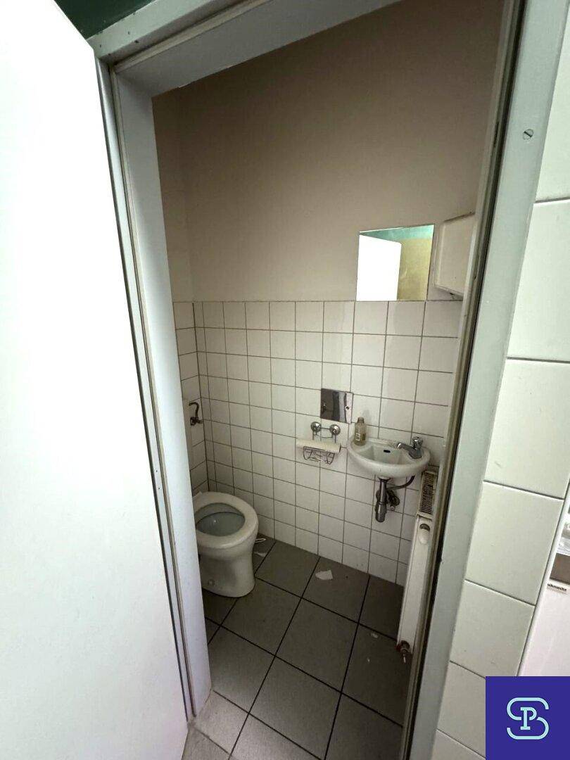 Kleiner Toilettenraum mit weißen Fliesen an den Wänden, einer Toilette und einem Waschbecken.