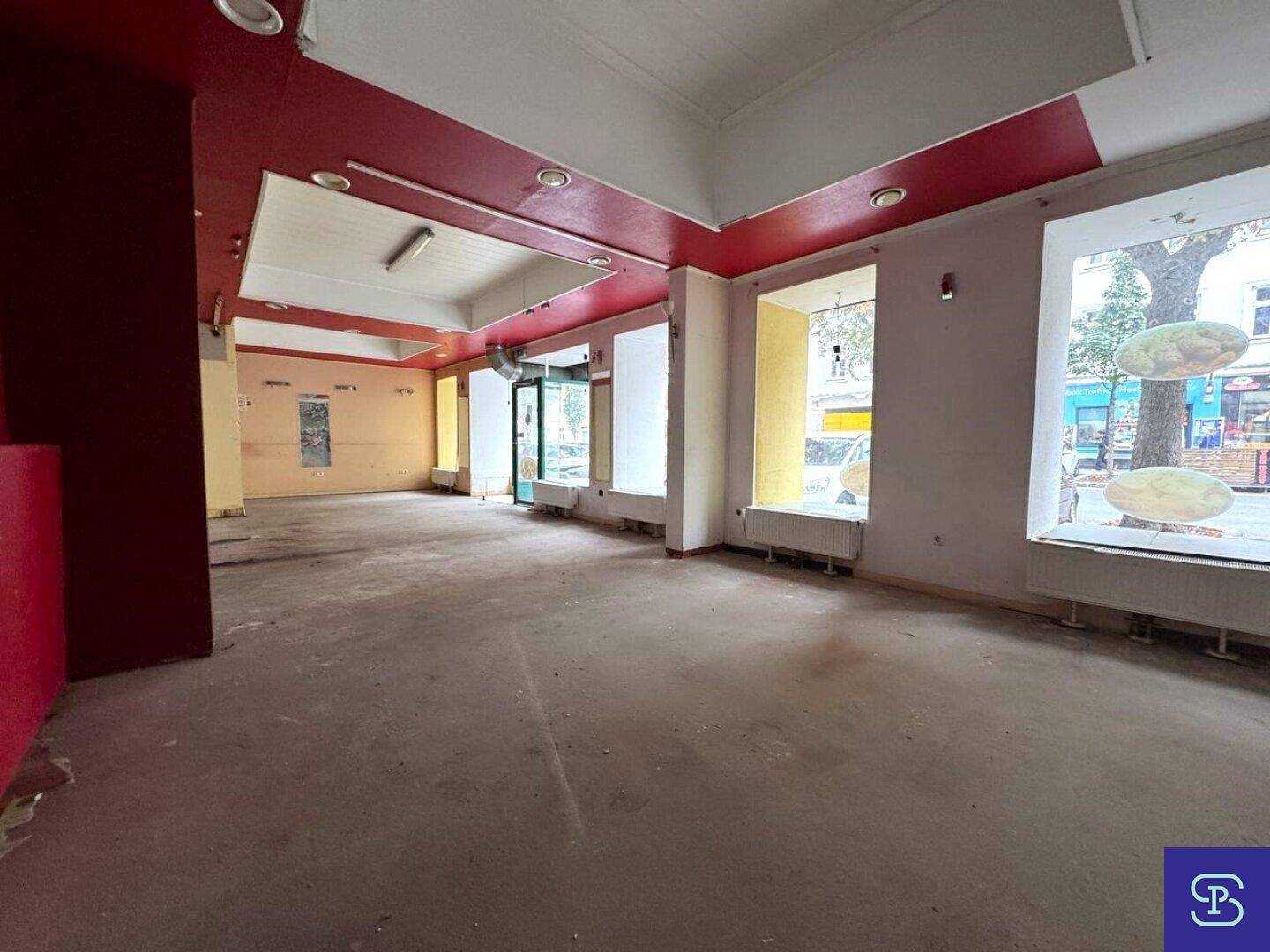 Großer, leerer Ladenraum mit Schaufenstern und roter Decke, ideal für Geschäftsumbau.