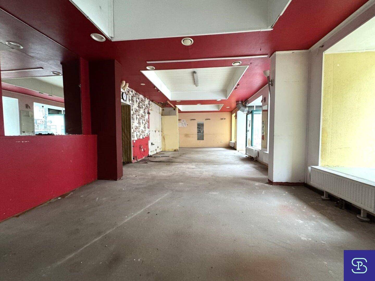 Weitläufiger Gewerberaum mit roter Decke und Blick auf die leeren Wände, bereit zur Gestaltung.