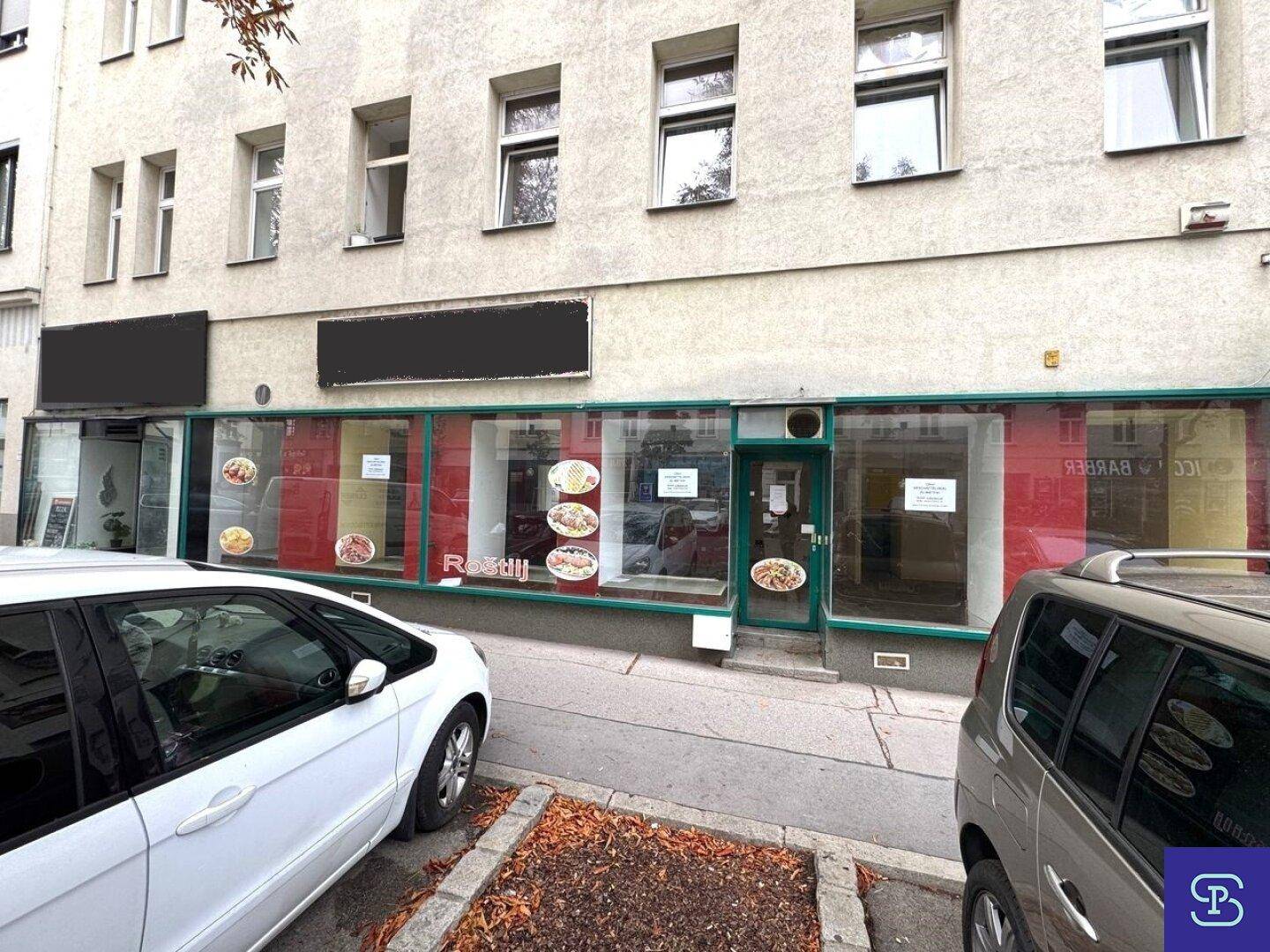 Fassade eines Geschäftsgebäudes mit großen Schaufenstern und parkenden Autos davor.